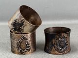 three antique silver napkins and a silver cup on a white surface
