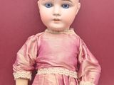an old doll with blue eyes and a pink dress on a red surface