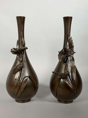 pair of bronze vases with leaves on them on a white background