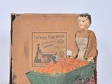 toy figurine of a woman with a cart of carrots in front of a box of carrots