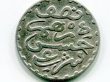 une vieille pièce de monnaie portant une inscription en arabe, posée sur une surface blanche