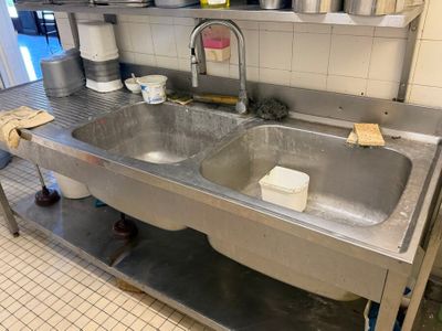 un évier en acier inoxydable dans une cuisine professionnelle, avec des casseroles et des poêles posées sur le plan de travail
