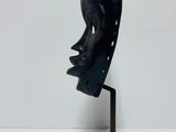 sculpture of a black mask on a metal stand against a white wall