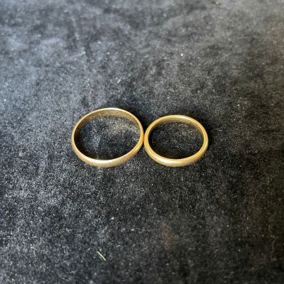 two gold wedding rings sitting on top of a black surface