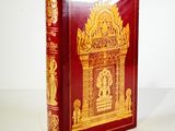 a red book with gold designs on it on a white surface