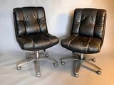 pair of black leather office chairs on casteors against a white backdrop