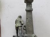 une statue représentant un homme debout à côté d'une horloge, posée sur un socle