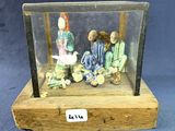 des figurines représentant trois personnes assises dans une vitrine posée sur un socle en bois