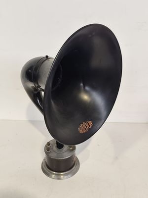 une enceinte noire de style ancien posée sur un pied métallique, elle-même posé sur une surface blanche
