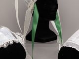 three mannequin heads wearing white bonnets with green ribbons
