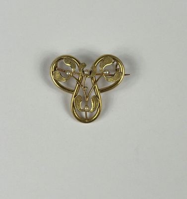 un gros plan d'une broche en or ornée de perles sur un fond blanc