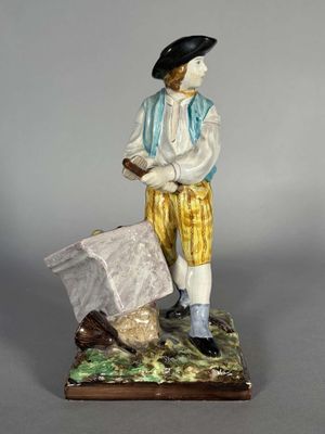 figurine représentant un homme coiffé d'un chapeau et vêtu d'un pantalon jaune, tenant un sac