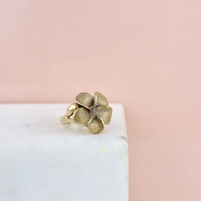 une bague en forme de fleur en or posée sur un bloc de marbre blanc