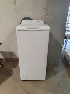 une machine à laver blanche posée dans une pièce, à côté d'une chaise