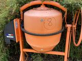 an orange cement mixer sitting in front of a bush