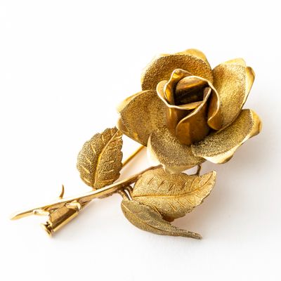 une rose dorée posée sur une surface blanche