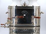 une cafetière ancienne en métal argenté, surmontée de deux tasses