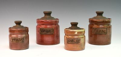 four brown jars with lids are lined up on a white surface