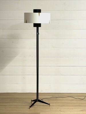 Le lampadaire est posé sur un parquet, devant un mur blanc.