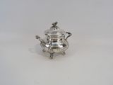 une théière ancienne en argent avec son couvercle, posée sur une surface blanche
