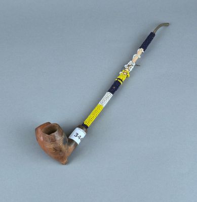 une vieille pipe avec un manche en bois et une poignée perlée sur un fond gris