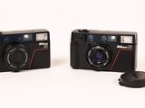 two cameras sitting next to each other on a white surface