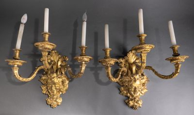 two gold wall sconces with white candles on a gray wall