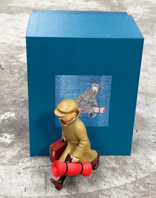 une figurine représentant un homme assis sur une valise rouge