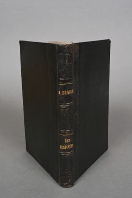 an old black book sitting on top of a table next to a white wall