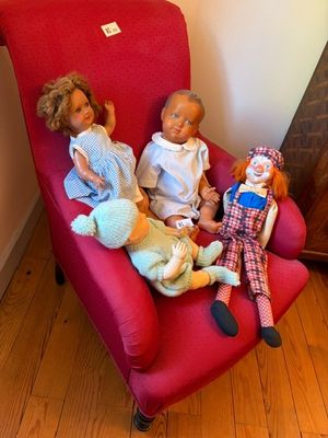 trois poupées assises sur une chaise rouge dans une pièce