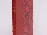 an old book with a red cover sitting on top of a white surface