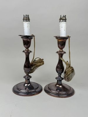 une paire de bougeoirs anciens en laiton, sur chacun desquels sont posées des bougies blanches