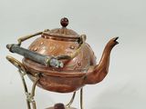 a small copper teapot on a stand next to a smaller copper teapot on a wooden stand