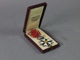 médaille dans un coffret en bois posé sur un support gris et orné d'un ruban rouge