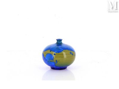 un petit vase bleu et vert posé sur une surface blanche