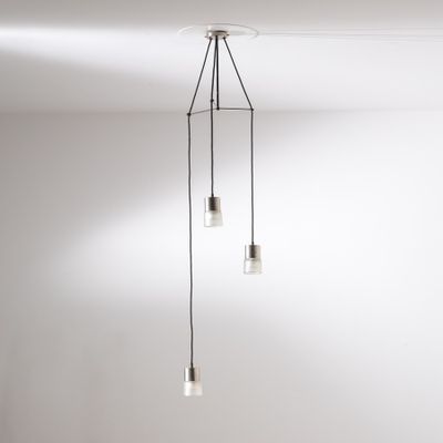 Trois suspensions en verre sont accrochées au plafond d'une pièce blanche