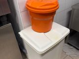 an orange bucket sitting on top of a white trash can