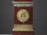 une horloge rouge et dorée posée sur une table blanche