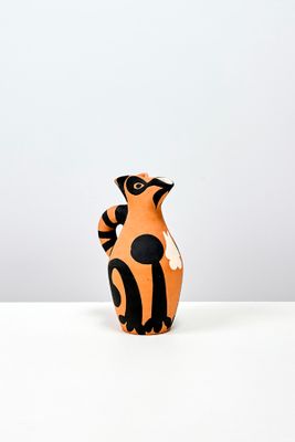 un petit vase orange et noir posé sur une table blanche