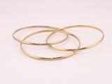 un ensemble de trois bracelets rigides dorés sur fond blanc