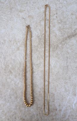deux colliers en or et une chaîne en or posés sur une surface en marbre