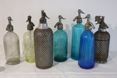 Plusieurs bouteilles en verre de différentes couleurs sont alignées sur une surface blanche.