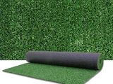 a roll of artificial grass next to a green hedge wall