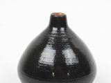 a black vase with a brown top sitting on a white surface