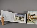 une main tenant un livre sur lequel figurent des illustrations de bateaux