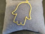 un petit pendentif en forme de main de Hamsa en or posé sur un oreiller
