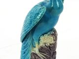 peacock figurine sitting on top of a tree stump on a white background