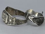 pair of silver bracelets on a gray surface with a white background