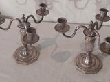 deux chandeliers en argent posés sur une table, avec un mur blanc en arrière-plan