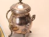 a silver tea pot and a silver spoon on a table